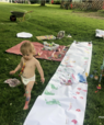 Image of two children playing outside with paint on a long white cloth. 